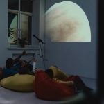 Vaikas su didinamuoju stiklu gamtoje tyrinėja augalus