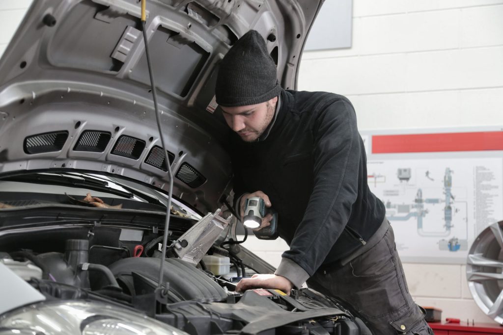 Mechanic inspecting a car engine during winter to identify the source of increased engine noise.