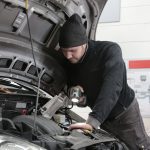 Mechanic inspecting a car engine during winter to identify the source of increased engine noise.