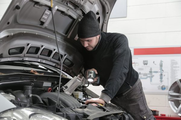 Mechanic inspecting a car engine during winter to identify the source of increased engine noise.