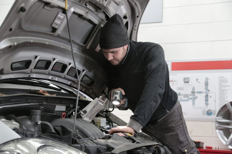 Mechanic inspecting a car engine during winter to identify the source of increased engine noise.